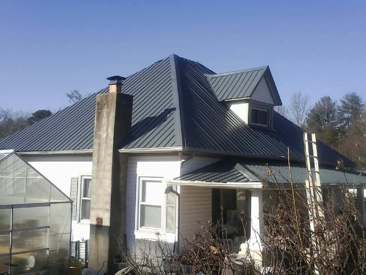 Dark blue standing seam metal roof on a white farmhouse with dormer — Slate & Tile Roof Repair by Roofing Brothers in Salix