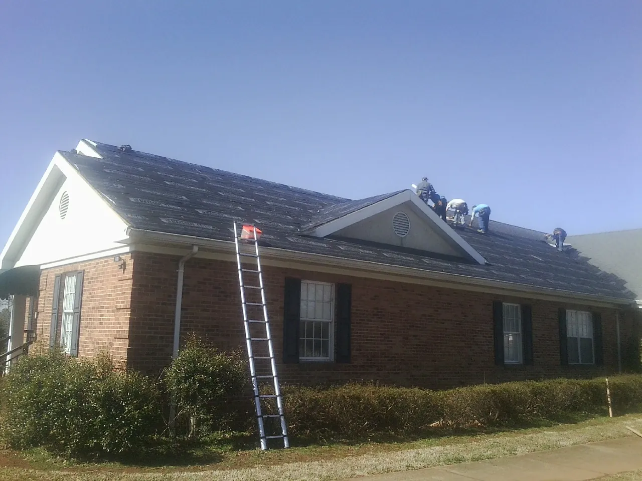 Crew tearing shingles off a brick ranch roof with a ladder set — Metal Roof Repair work by our crew in Salix