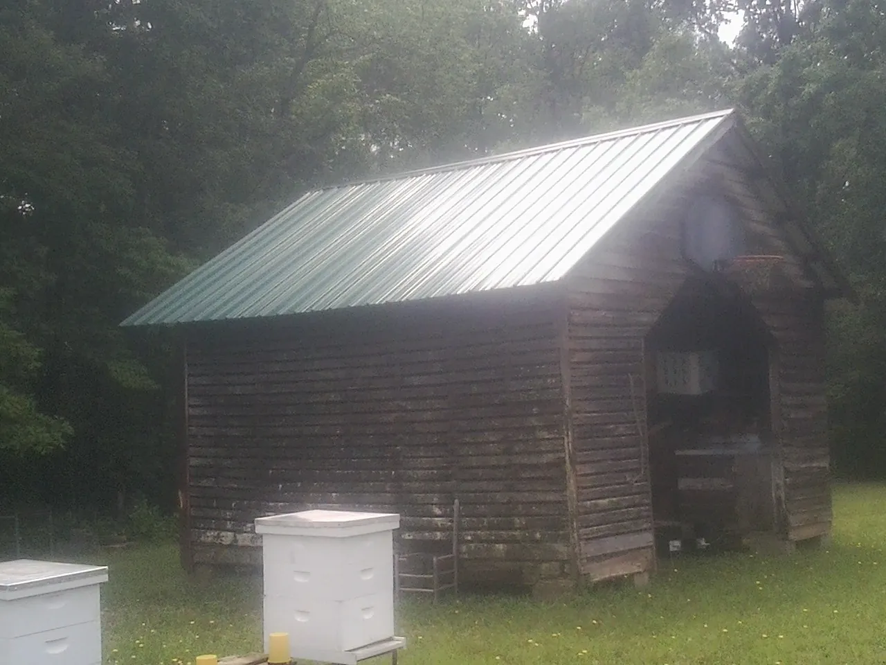 Green metal roof on a weathered barn beside stacked beehives in Salix