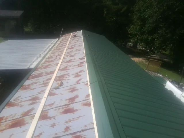 Old rusted panels beside newly installed green metal roofing — Wind Damage Roof Repair by Roofing Brothers in Salix