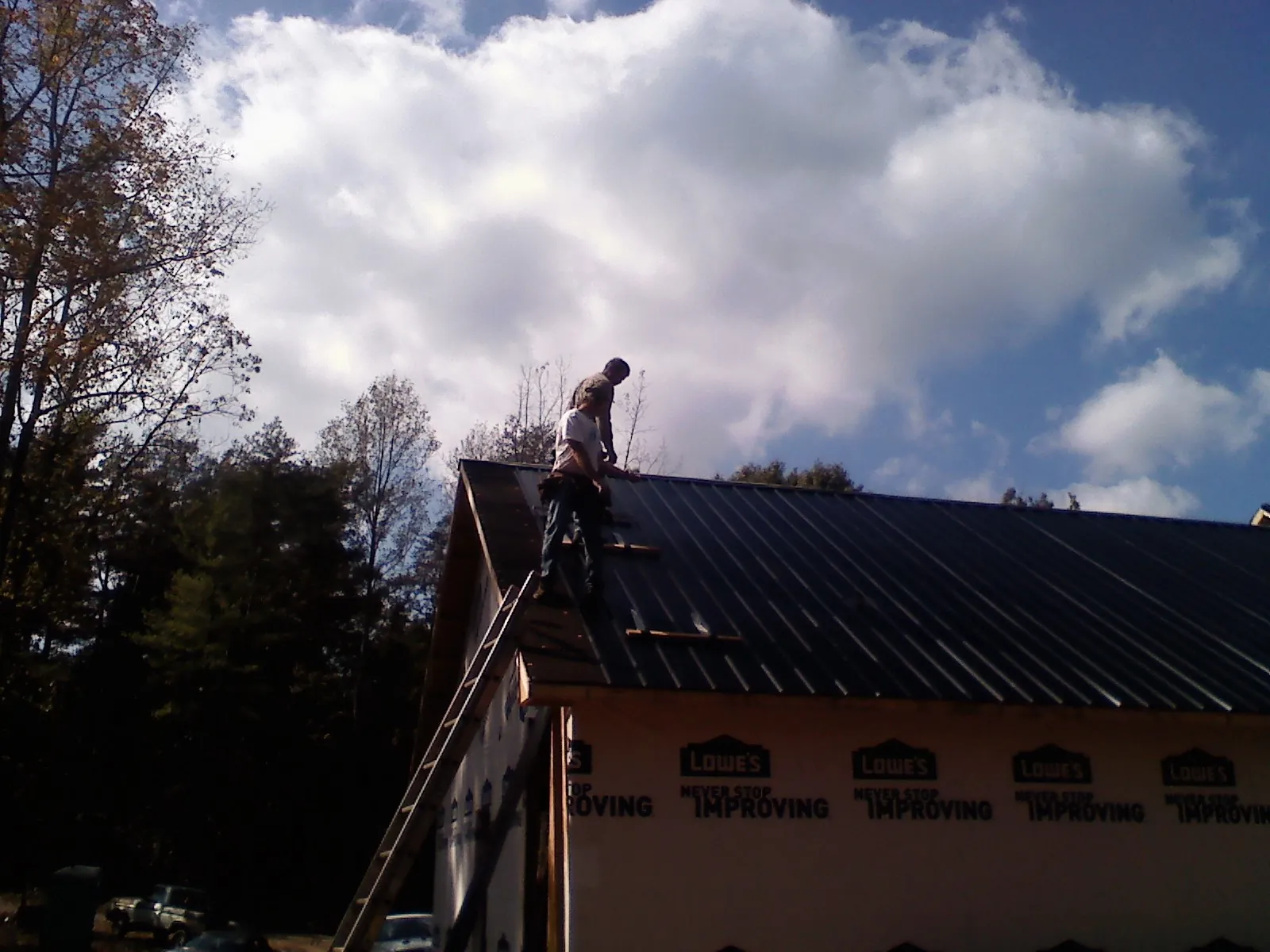 Roofer fastening dark metal panels high against a cloudy sky, from a Roof Inspection job in Salix