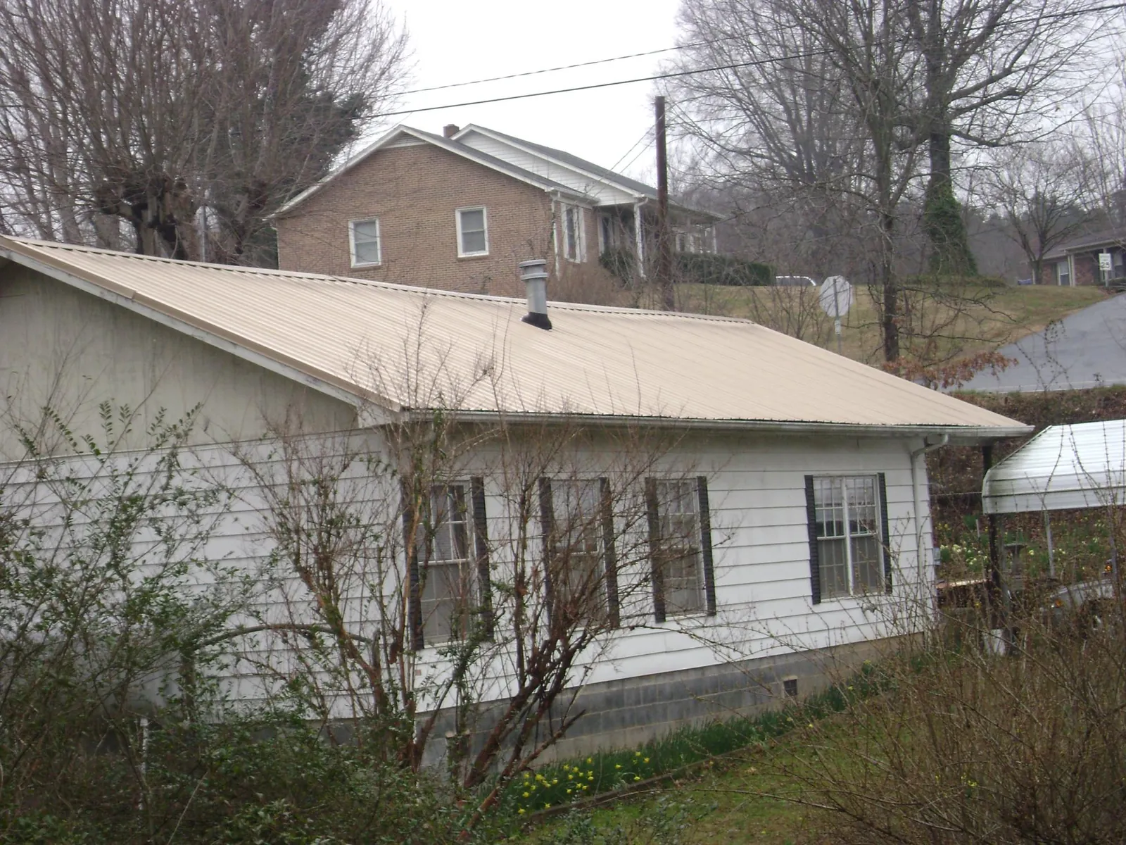 Tan metal roof on a white sided house set into a hillside — Commercial Roofing by Roofing Brothers in Salix